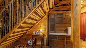 A wooden interior with a sloped ceiling, a staircase, a small table with a lamp, and wooden cabinets. - Walk to Elk Rapids + Steps from East GT Bay (Elk Rapids)