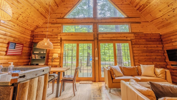 A log cabin interior with a dining area, sofa, and a large window. - Walk to Elk Rapids + Steps from East GT Bay (Elk Rapids)