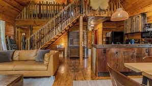 A wooden cabin interior with a staircase, a sofa, a dining table, and a kitchen area. - Walk to Elk Rapids + Steps from East GT Bay (Elk Rapids)