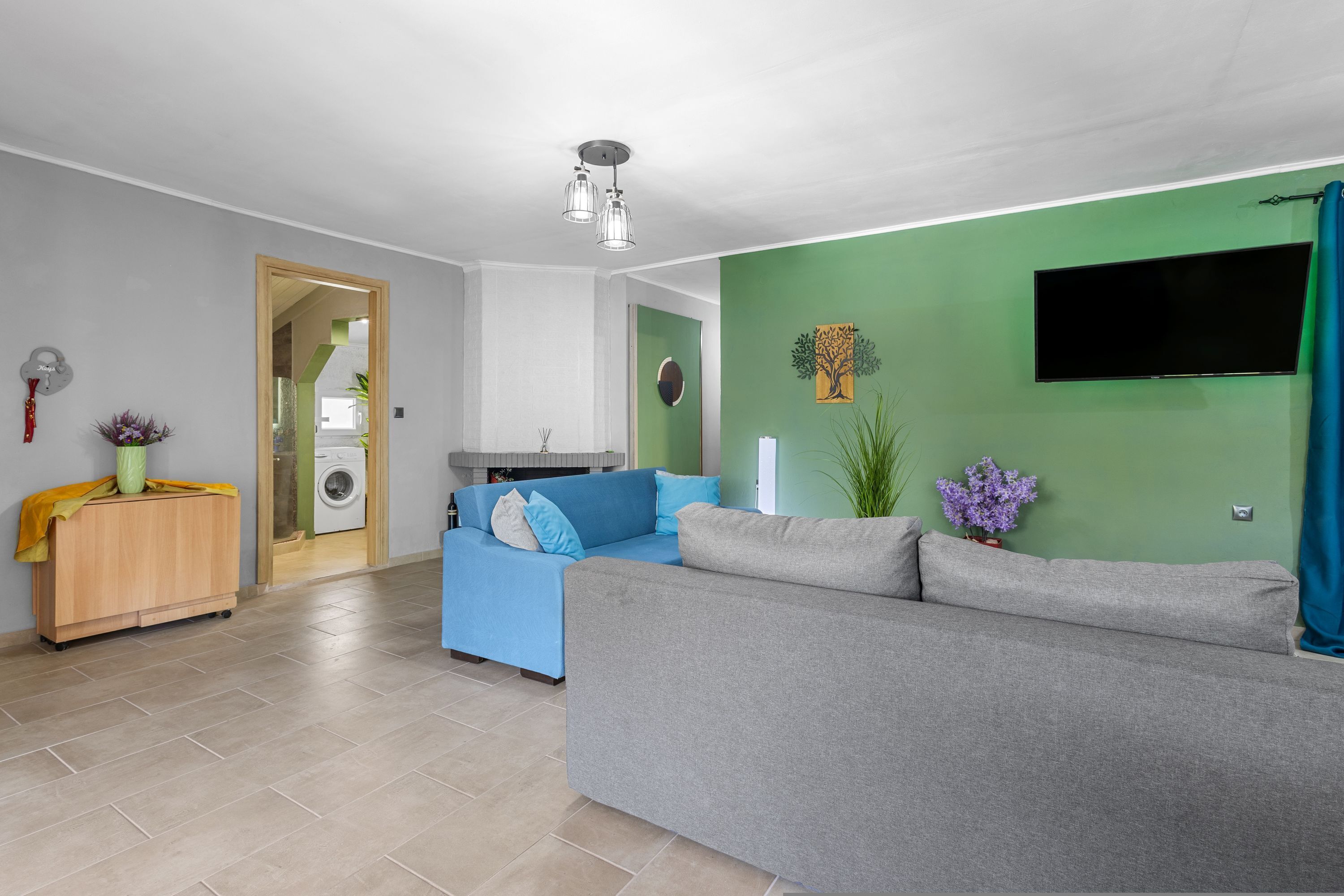 A living room with a grey sofa, a blue sofa, a wooden cabinet, a TV, and a green wall.