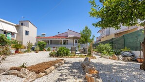 Ein Wohngebiet mit einem Haus, das ein rotes Ziegeldach, eine überdachte Terrasse und einen Garten mit verschiedenen Pflanzen sowie einen Schotterweg hat.