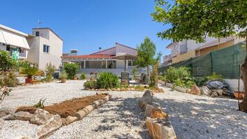 A residential area with a house featuring a red-tiled roof, a covered patio, and a garden with various plants and a gravel driveway.