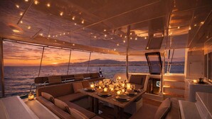 Interior luxuoso de um iate, com área de refeições, assentos confortáveis e vista para o mar ao pôr do sol.