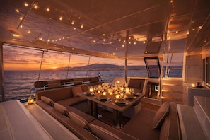 Interior lujoso de un yate, con zona de comedor, asientos cómodos y vista al mar al atardecer.