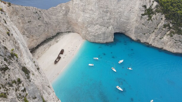Paisagem costeira com um penhasco imponente, uma praia de areia e vários barcos na água.