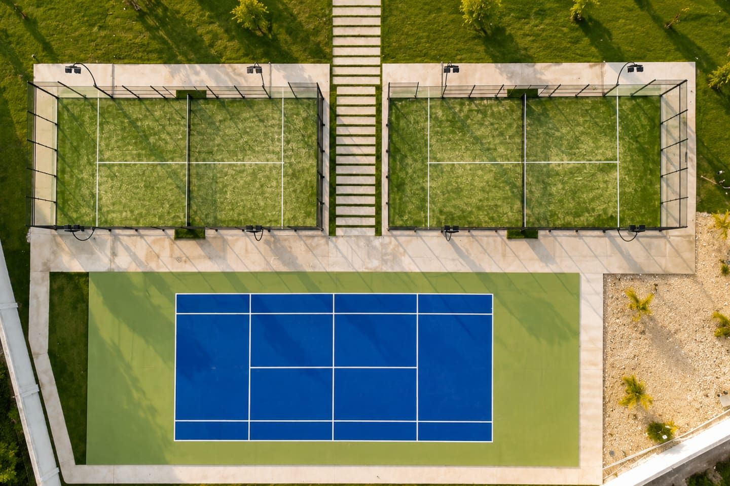 An aerial view of a tennis court with two adjacent courts, a central walkway, and surrounding greenery.