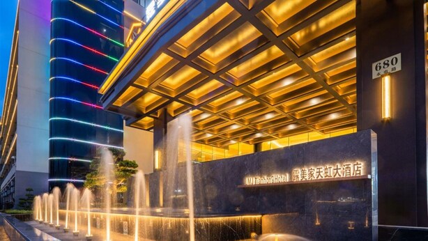 Entrada de hotel con fuente de agua, señalización iluminada y diseño arquitectónico moderno.