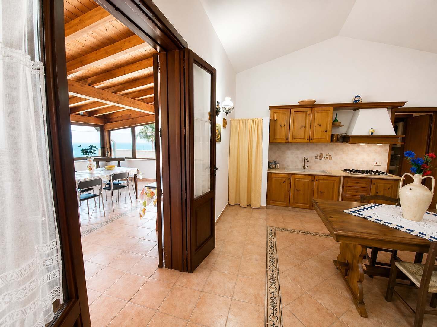 A kitchen with wooden cabinets, a dining table, and a view to the outside.