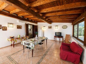 A dining area with a wooden ceiling, a table with a floral tablecloth, a red sofa, and a television on a stand. - Villa Andromaca SP Living Solutions (san vito lo capo)