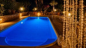 A swimming pool with a stone border, surrounded by potted plants and outdoor lighting. - Villa Verabetta (Piano di Sopra)