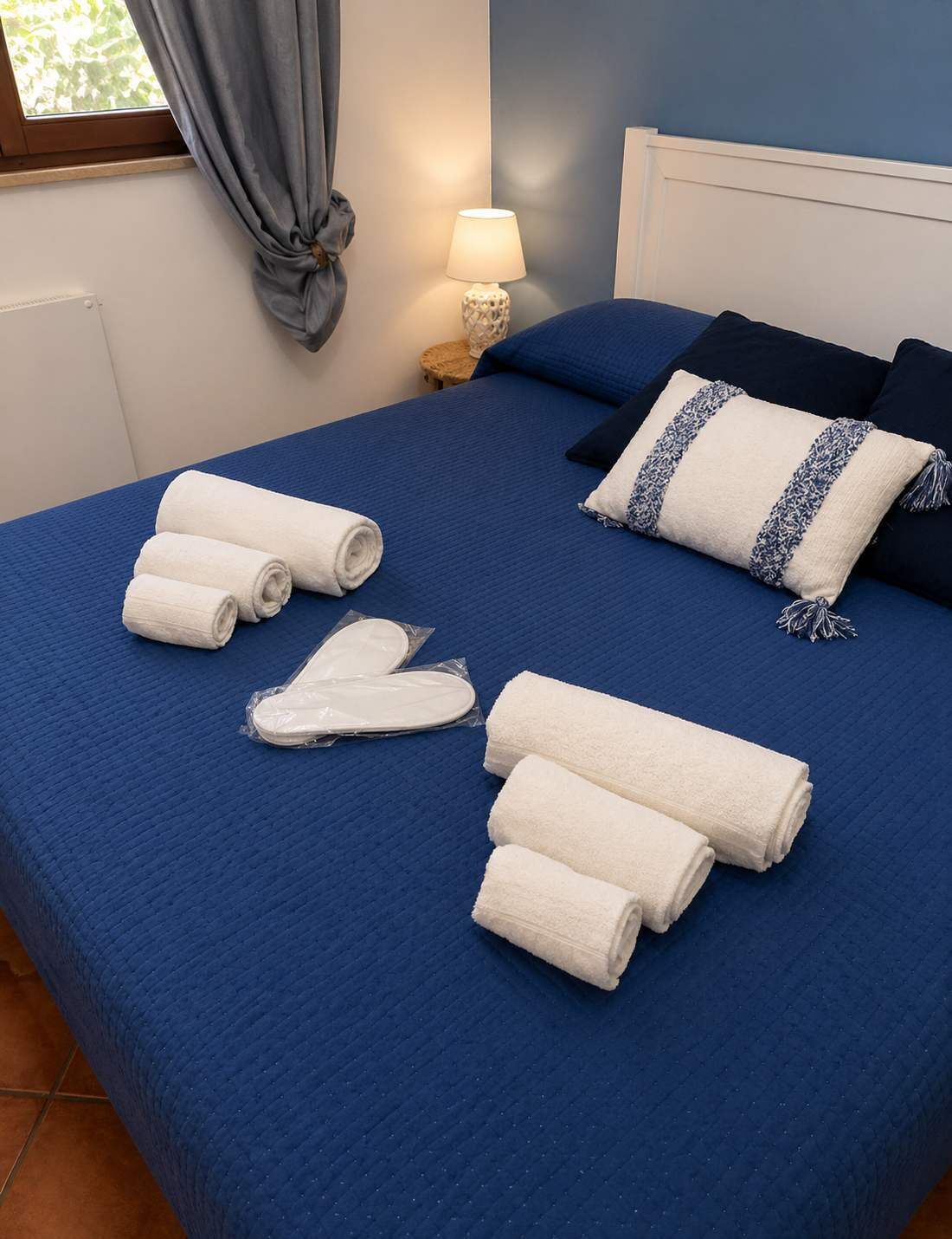 A neatly made bed with blue bedding, white towels, and a pillow with a blue and white pattern.