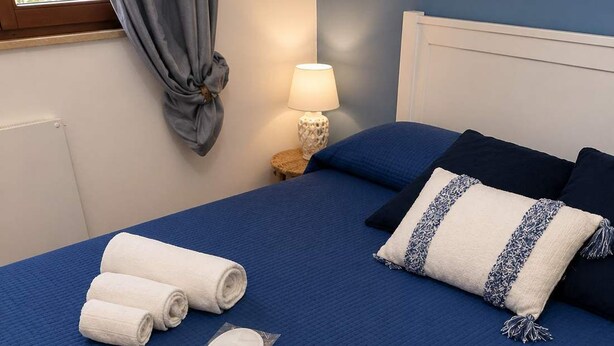 A neatly made bed with blue bedding, white towels, and a pillow with a blue and white pattern. - Villa Verabetta (Piano di Sopra)