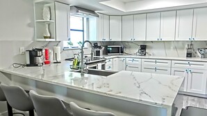 Una cocina moderna con armarios blancos, una isla de mármol y taburetes de bar.