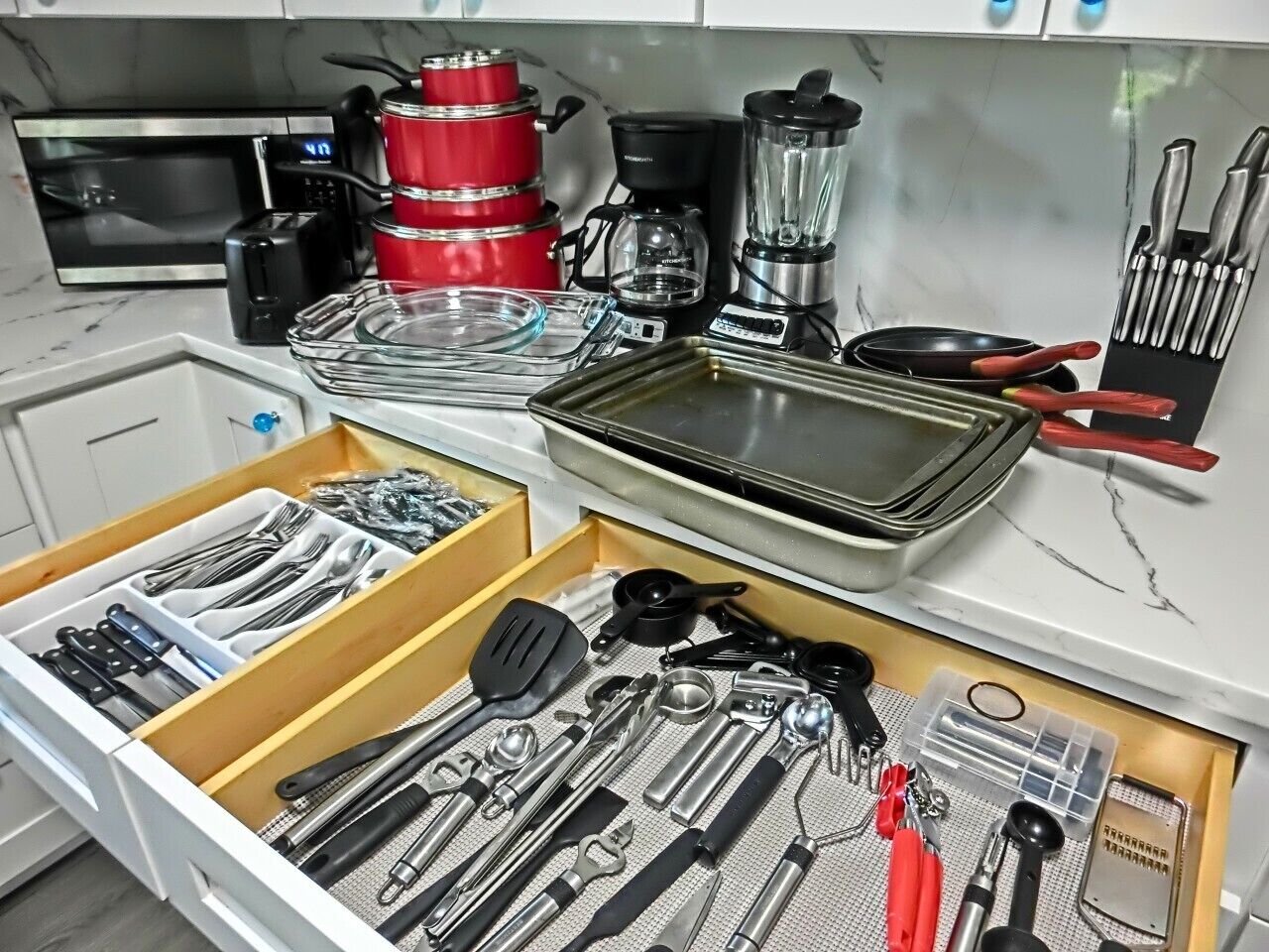 A kitchen with a microwave, toaster, coffee maker, blender, and various utensils in drawers.