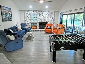 Ein Wohnzimmer mit einem Kicker, blauen und orangen Sofas, einem Kamin und einem großen Fenster.