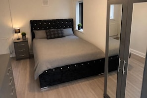 Une chambre à coucher avec un lit, des tables de chevet, une fenêtre et un miroir.