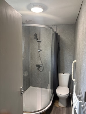 Un baño con cabina de ducha, inodoro y una tubería visible en la pared.