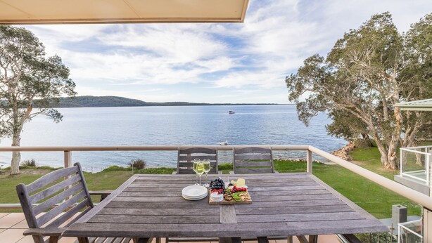 Una mesa de madera con vistas a un lago, un barco a lo lejos y una zona verde con árboles.