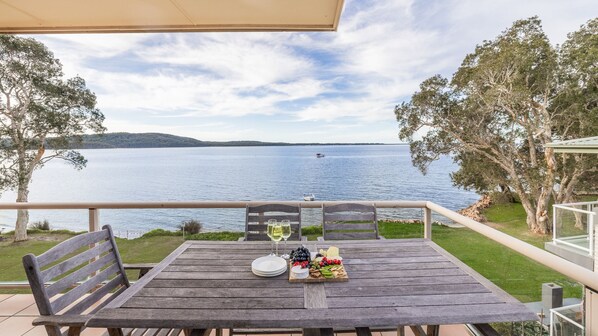 A wooden table with a view of a lake, a boat in the distance, and a grassy area with trees. - Pelican Sands, 4/83 Soldiers Point Road (Soldiers Point)