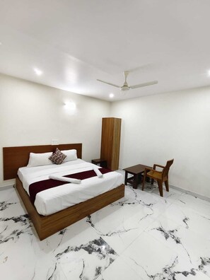A neatly arranged bedroom with a bed, bedside table, chair, and a desk with a chair. - Hotel Relax inn (Chikkamagaluru)