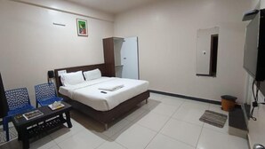 Un dormitorio con cama, escritorio, sillas, televisor y ventilador de techo.