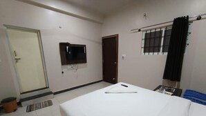 Una habitación de hotel con una cama, un televisor en la pared, una puerta y una ventana con cortinas.