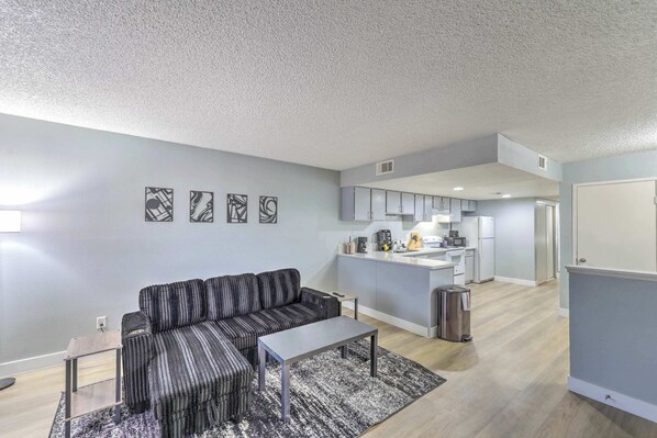 A modern living room with a sofa, a coffee table, and a rug. There is a kitchen area with cabinets and a countertop. - Relax in Comfort! Sleeps 6! (Las Vegas)