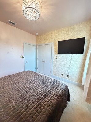 A bedroom with a bed, a wardrobe, a television mounted on the wall, and a ceiling light fixture. - The Carriage House - 5 BEDROOMS / SLEEPS 16 / 1 MILE FROM ACU (Abilene)