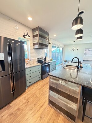 A modern kitchen with a stainless steel refrigerator, a built-in oven, and a large island with a sink. - The Carriage House - 5 BEDROOMS / SLEEPS 16 / 1 MILE FROM ACU (Abilene)