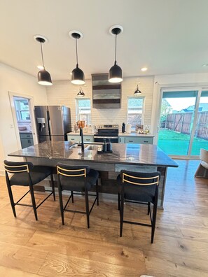 A modern kitchen with a large island, pendant lights, and a view to the backyard.