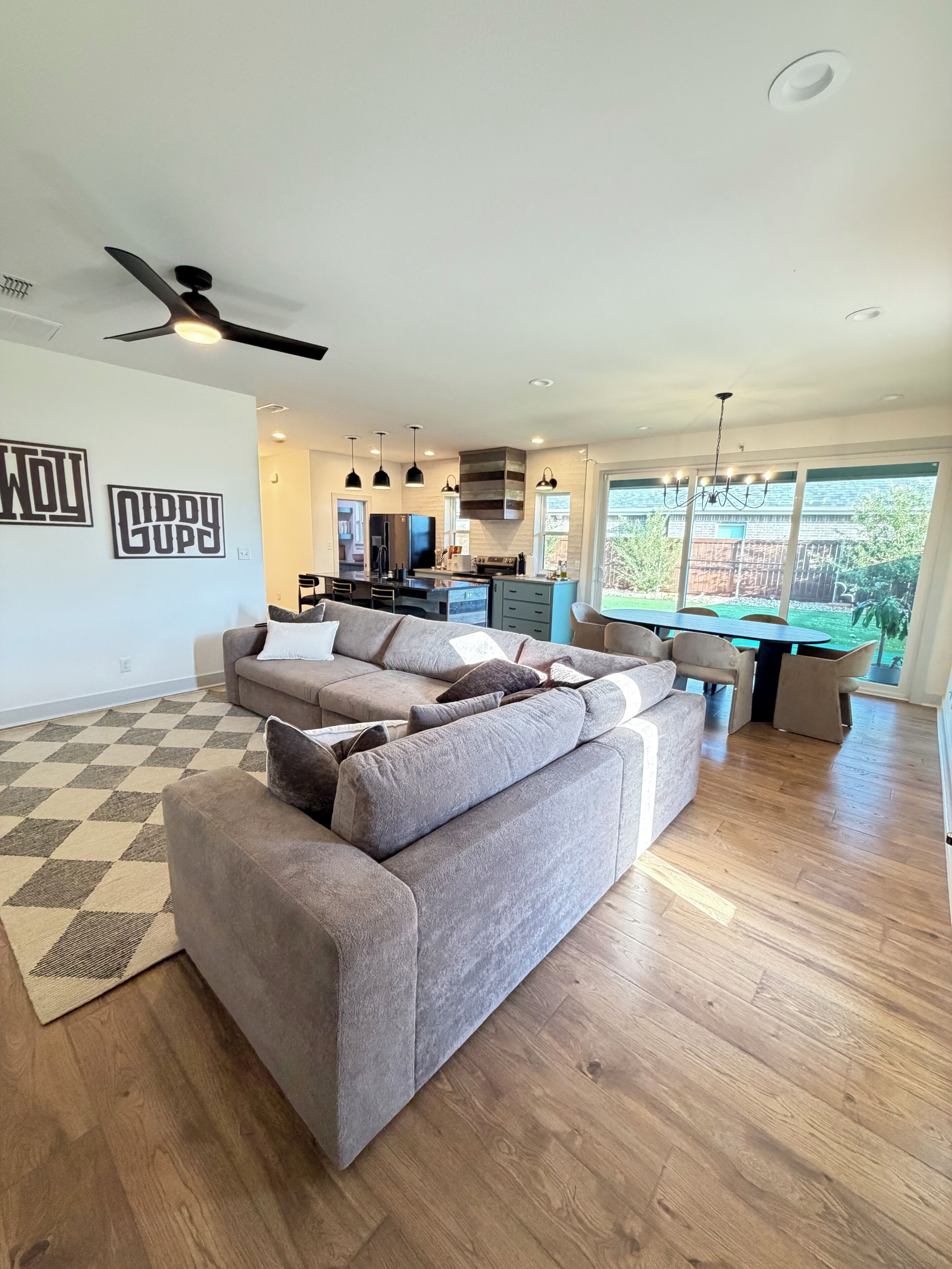 A modern living room with a large sectional sofa, a kitchen area with a built-in island, and a dining area with a table and chairs.