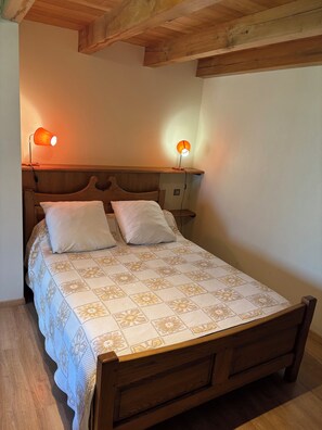 Een houten bed met een bedovertrek met patroon, twee bedlampjes en een houten hoofdeinde.