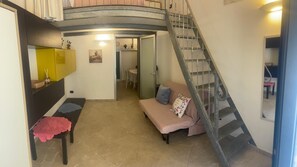 Ein Wohnzimmer mit einer Couch, einem Tisch mit roter Decke, einer Treppe und einem gelben Schrank.