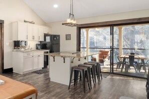 A modern kitchen with white cabinets, a central island, bar stools, and a dining area with a view. - Family-friendly, waterfront, 2-bedroom condo inside Rumbling Bald, on Lake Lure (Lake Lure)