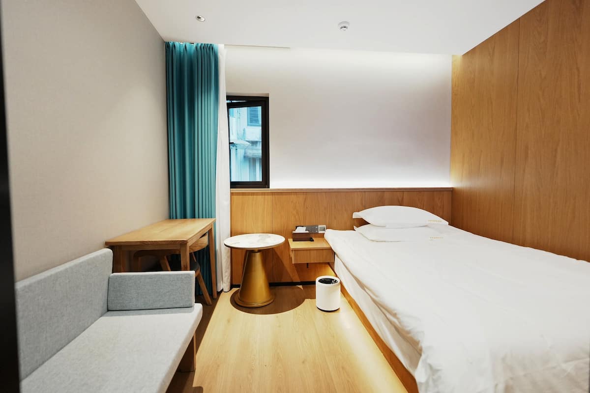 Ein modernes Hotelzimmer mit einer Couch, einem kleinen runden Tisch, einem Nachttisch, einem Bett und einem Fenster mit Vorhängen.