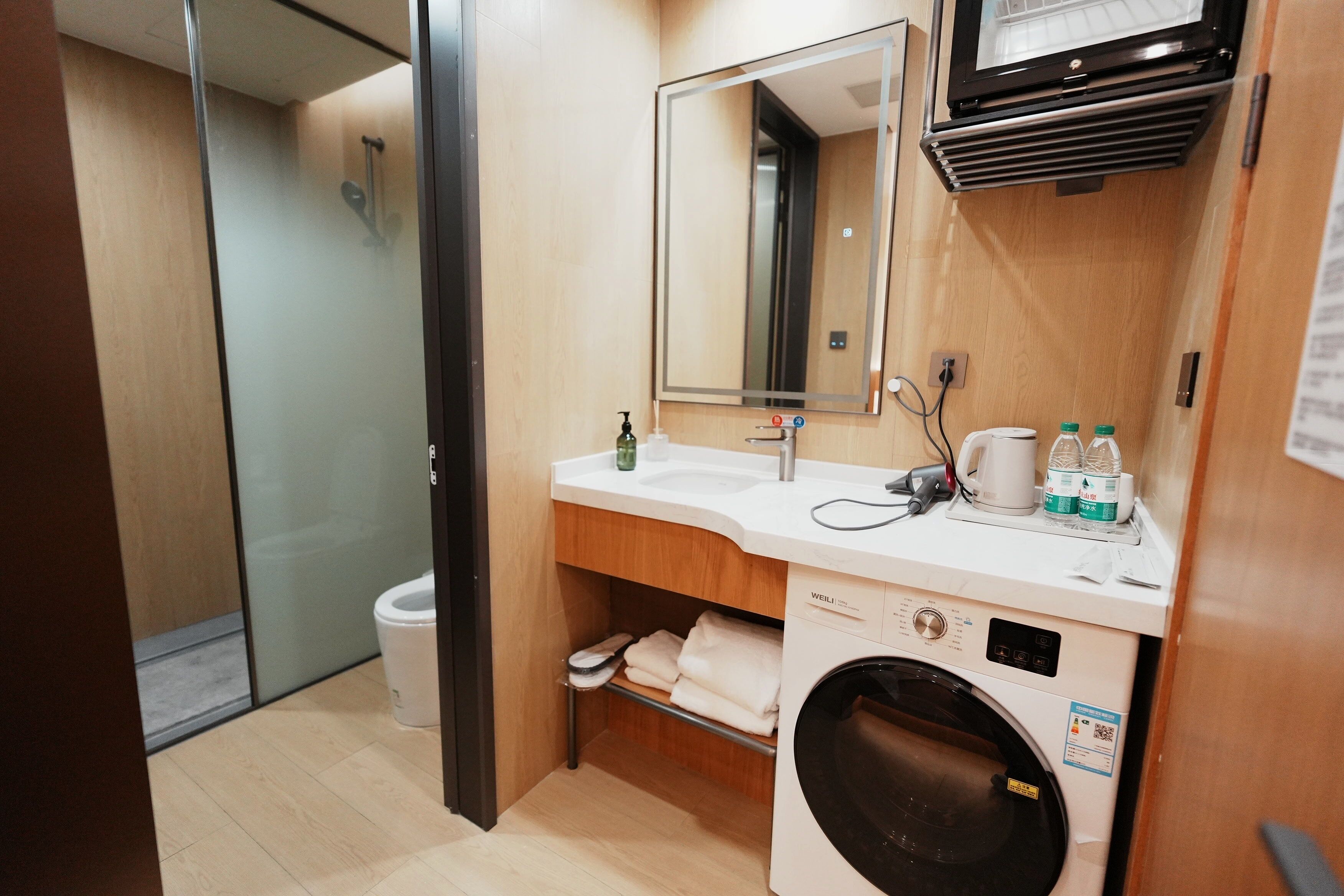 Un baño de hotel pequeño con lavamanos, espejo y lavadora.