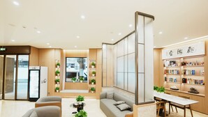 A modern hotel lobby with seating, a reception desk, a refrigerator, and a bookshelf with books and decorative items. - Shanghai Weikesun Business Hotel (Shanghai)