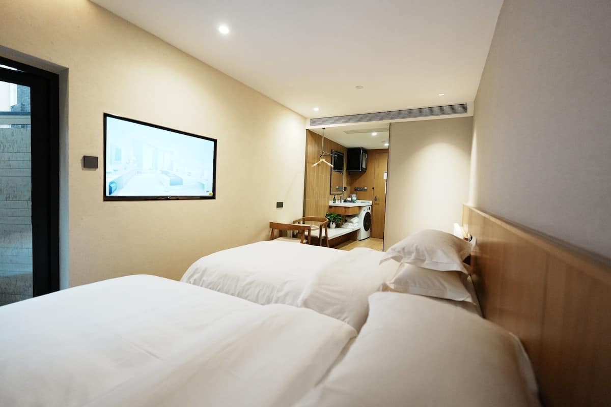 Ein Hotelzimmer mit zwei Betten, einem an der Wand befestigten Fernseher, einem kleinen Tisch mit einem Stuhl und einem durch eine offene Tür einsehbaren Badezimmer.
