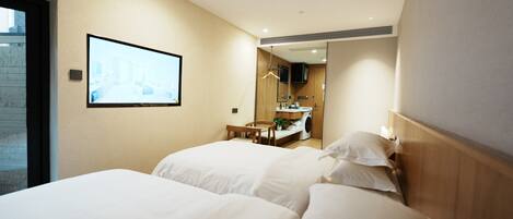 Ein Hotelzimmer mit zwei Betten, einem an der Wand befestigten Fernseher, einem kleinen Tisch mit einem Stuhl und einem durch eine offene Tür einsehbaren Badezimmer.