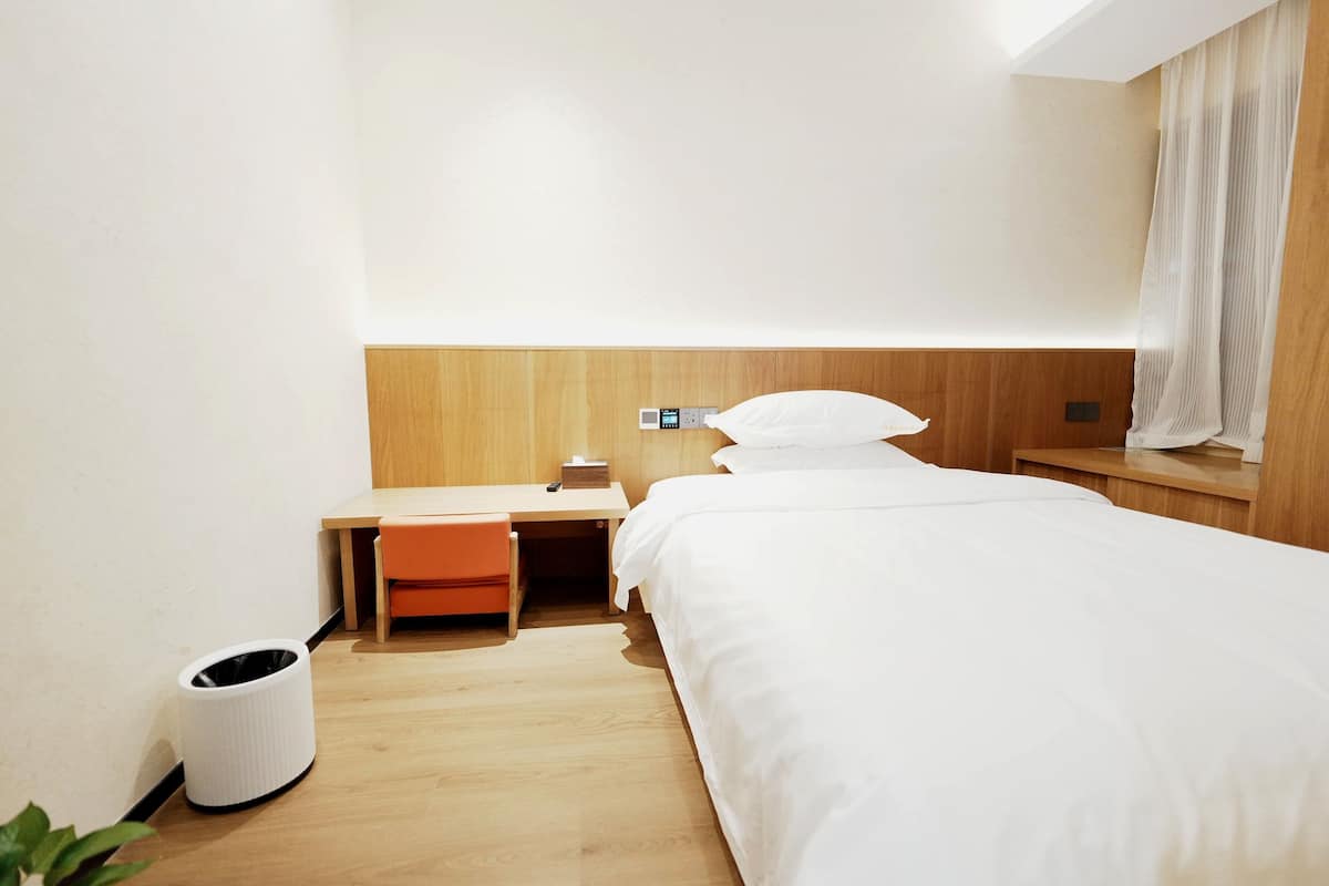 Ein Hotelzimmer mit Bett, Schreibtisch, Stuhl, Mülleimer und Nachttisch.