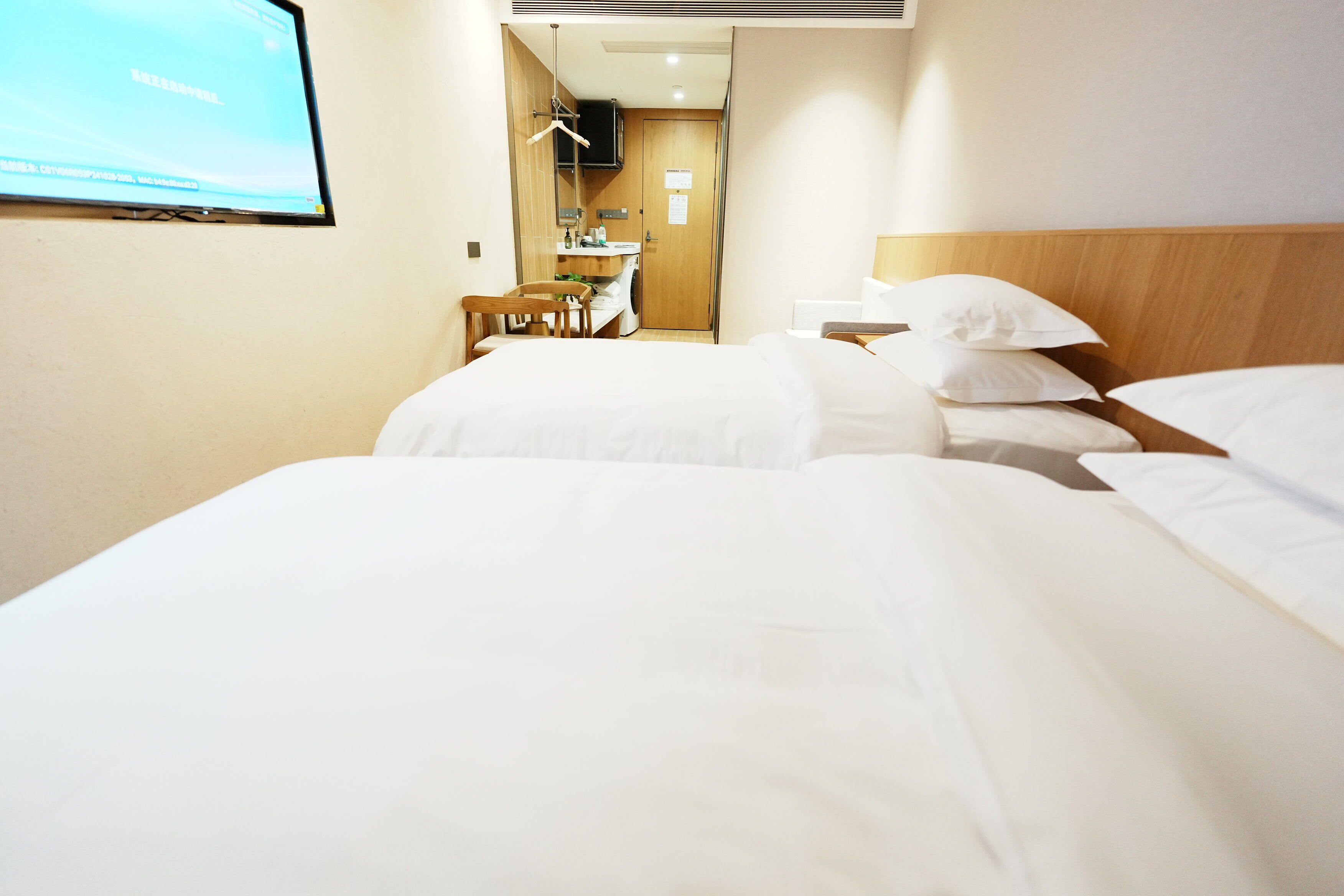 Een hotelkamer met twee bedden, een bureau, een stoel, een televisie en een badkamer die door een open deur zichtbaar is.