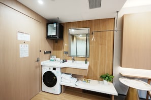 A modern bathroom with a washing machine, sink, mirror, and a small table with a plant.