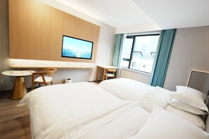 Ett hotellrum med en säng, en tv som är monterad på väggen, ett litet bord och en stol.