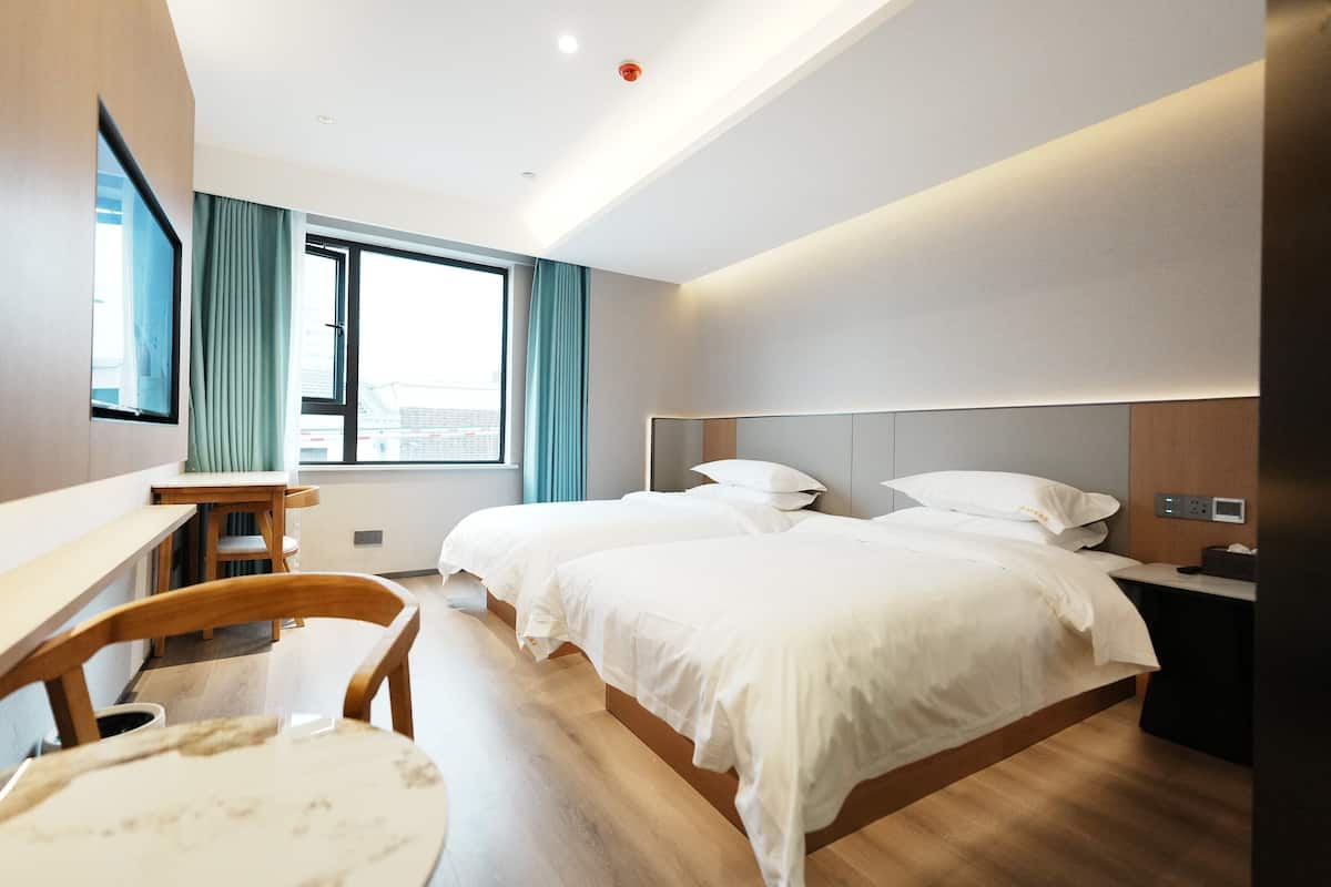 Ein Hotelzimmer mit zwei Betten, einem Schreibtisch, einem Stuhl und einem großen Fenster.