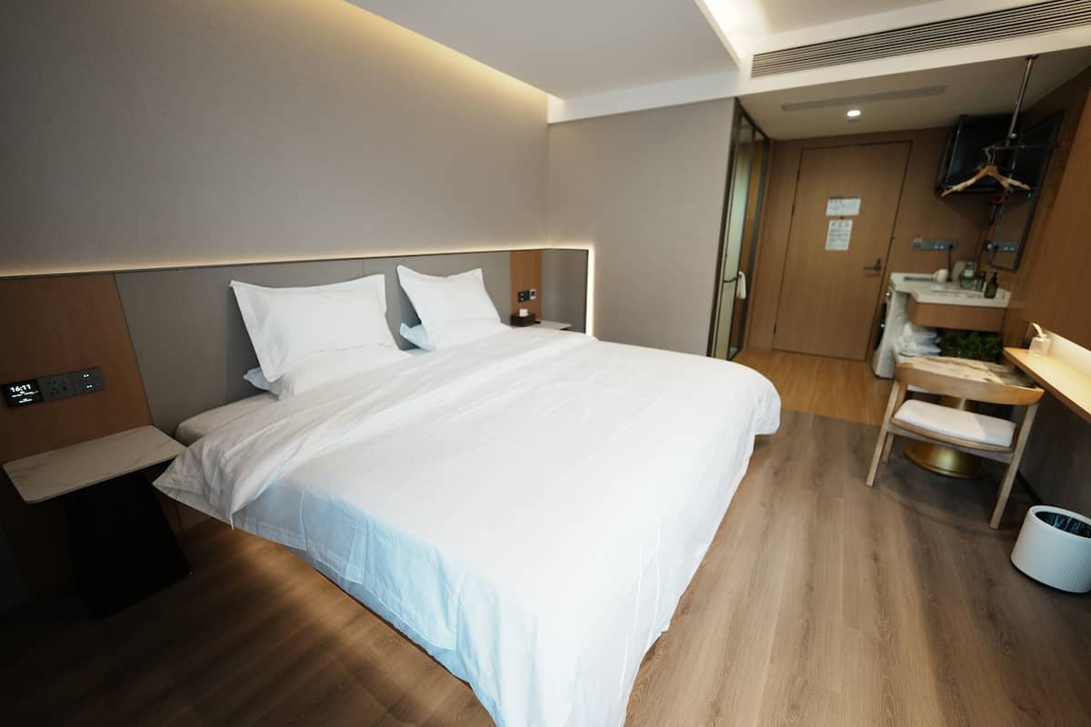 Ein modernes Hotelzimmer mit einem großen Bett, einem Nachttisch und einer kleinen Schreibtischzeile mit Stuhl.