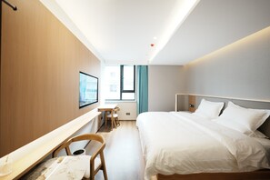 Quarto de hotel com uma cama, escrivaninha, cadeira e janela.