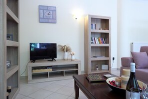 A living room with a TV, bookshelf, and a coffee table with a board game and candles. - Serene Apartment Lefkada (Lefkada)