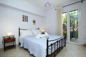 A bedroom with a bed, bedside tables, a lamp, and a view through a sliding glass door. - Serene Apartment Lefkada (Lefkada)