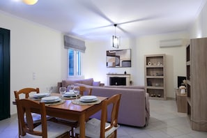 A dining area with a wooden table set for four, a sofa, and a bookshelf. - Serene Apartment Lefkada (Lefkada)
