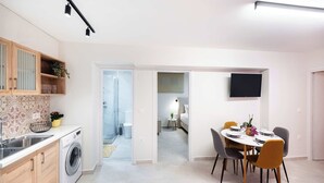 Une cuisine moderne équipée d’un lave-linge, un coin repas avec une table et des chaises, et une chambre avec un lit et une télévision.